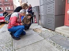 Personen hocken vor den frisch eingesetzten Stolpersteinen im Kopfsteinpflaster