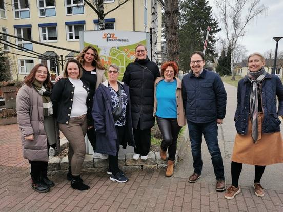 Gruppenbild 7 Personen 6 Frauen 1 Mann vor Schild