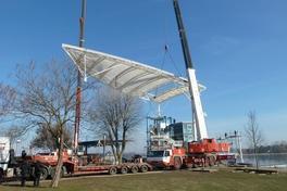 An zwei Kranauslegern schwebt die Dachkonstruktion in die Höhe.