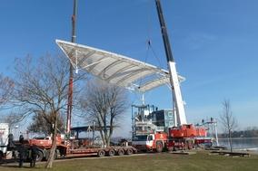 An zwei Kranauslegern schwebt die Dachkonstruktion in die Höhe.