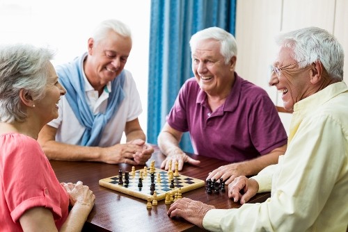 4 Senioren spielen lachend Brettspiele